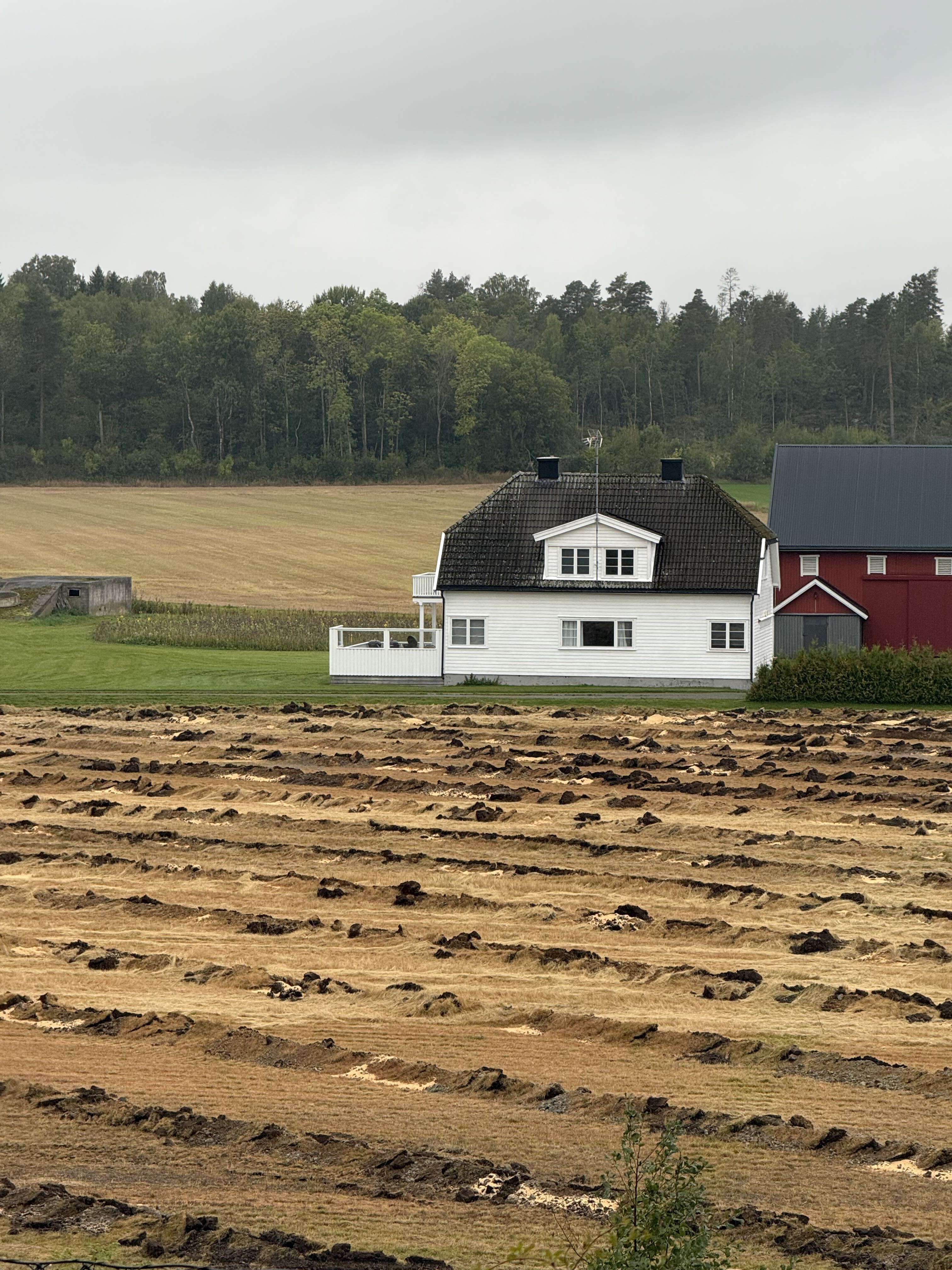 Hvitt våningshus, rød driftsbygning og jorder ved en norsk gård.